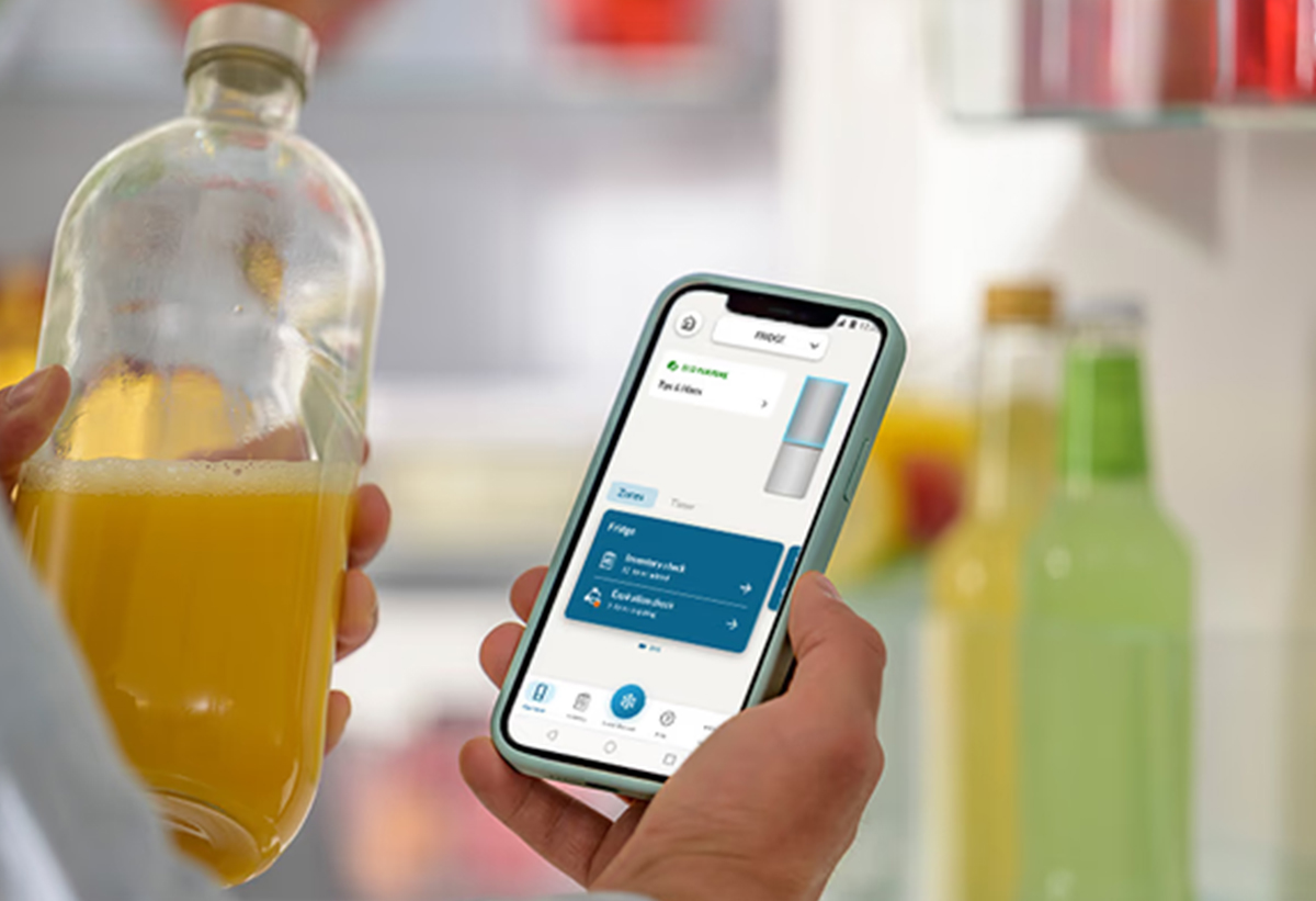 Απεικονίζεται άτομο να κρατάει ένα κινητό με ανοιχτή την εφαρμογή και μισό μπουκάλι χυμό.